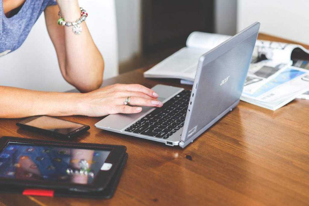 Close up of woman with one hand typing on a laptop and the other hand out of the shot