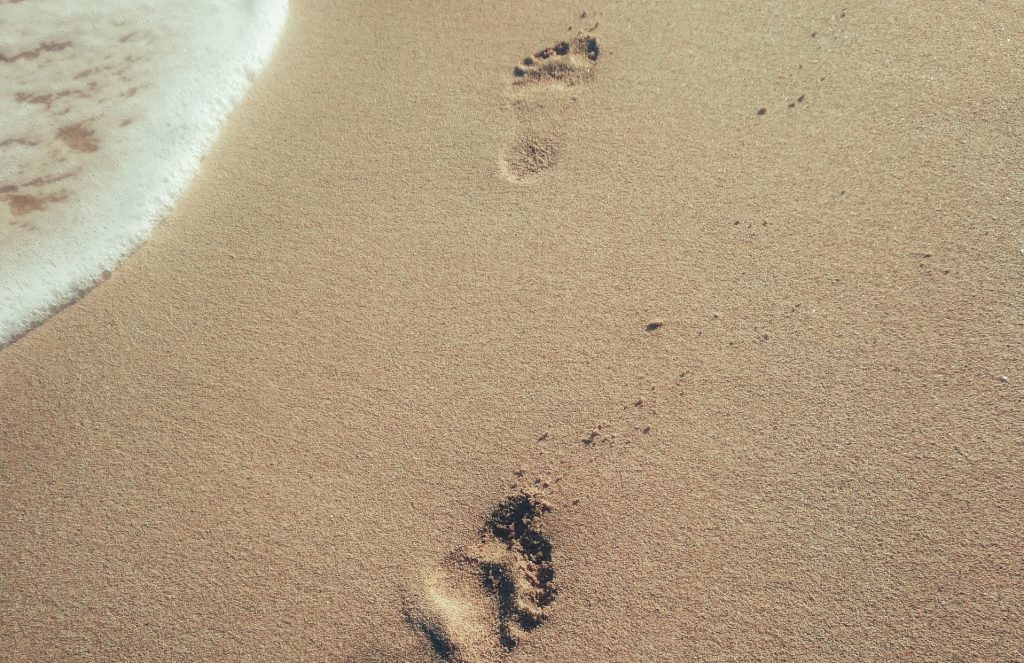 sand beach with two footprints in the sand from someone walking and ocean water on the left