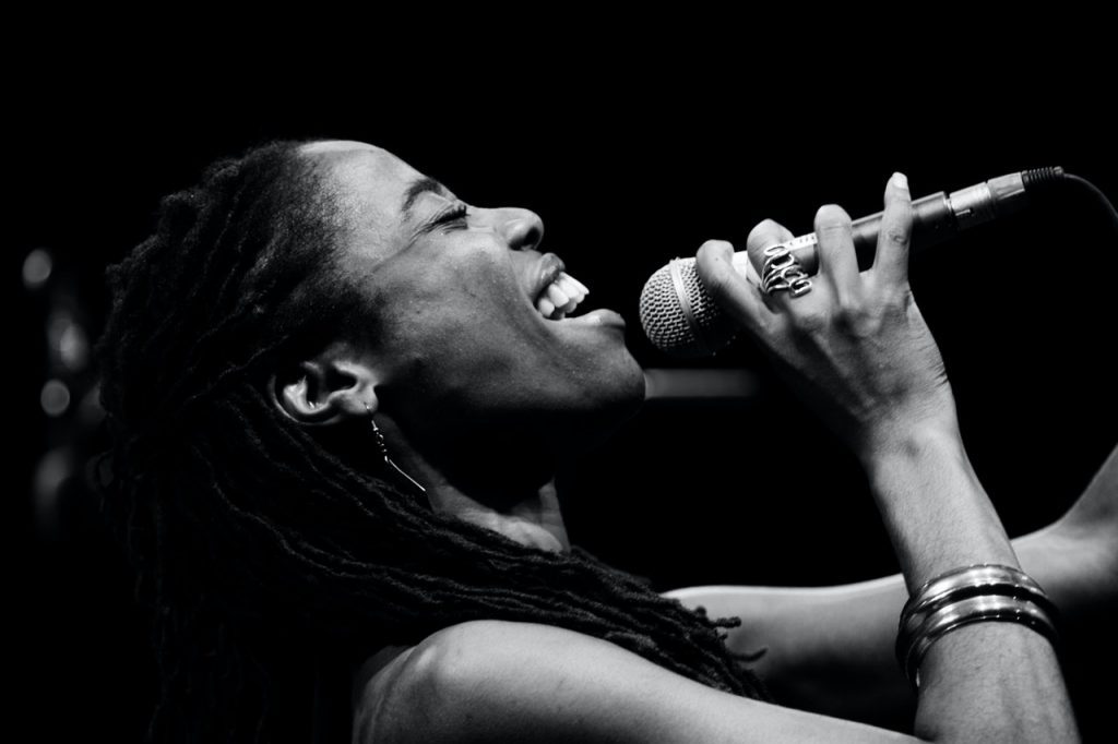 black and white image of a closeup of woman from shoulders up. she is in profile to the right and holding a microphone up to her smiling mouth