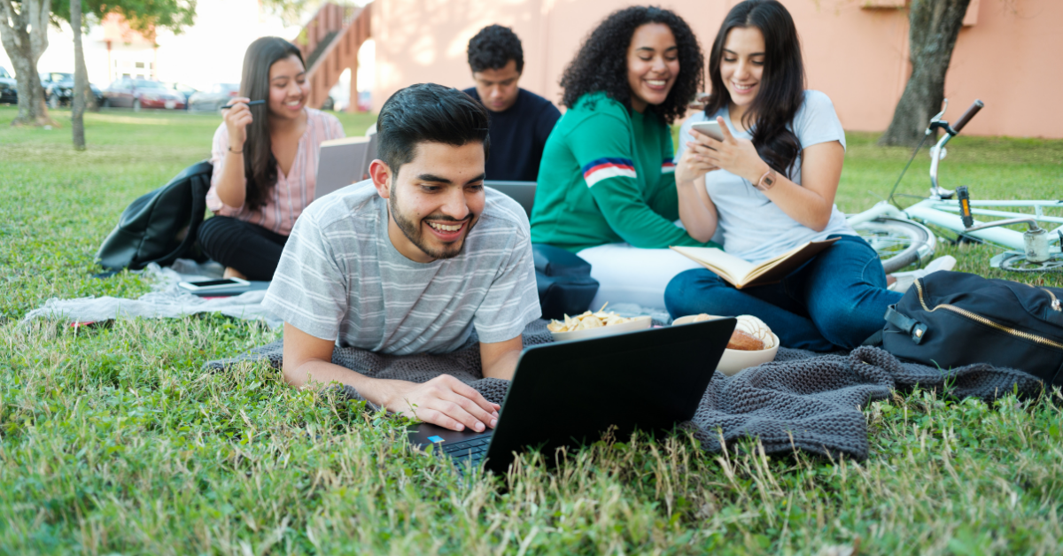 Group of young adults outside on grass studying.