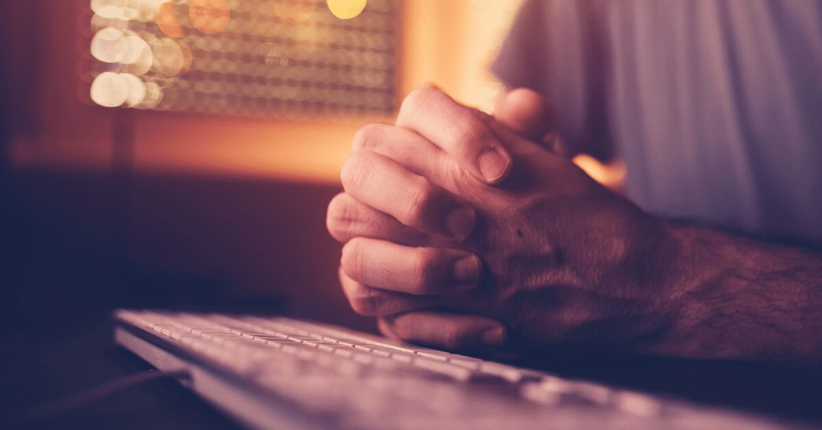 Hands in prayer at computer keyboard.