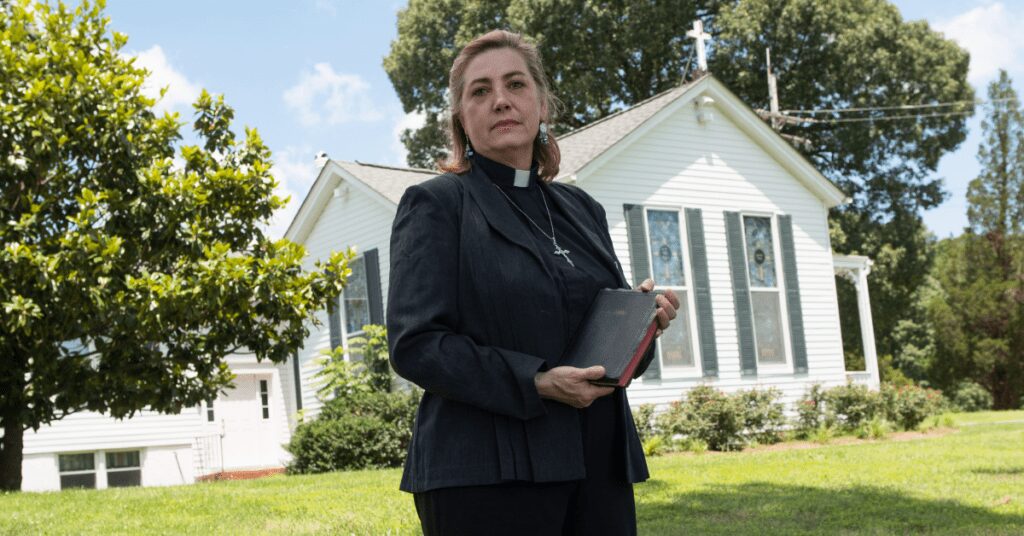 Woman pastor in front of church.