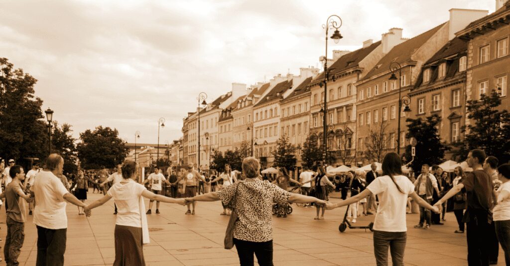 Circle of people outside holding hands on a street.