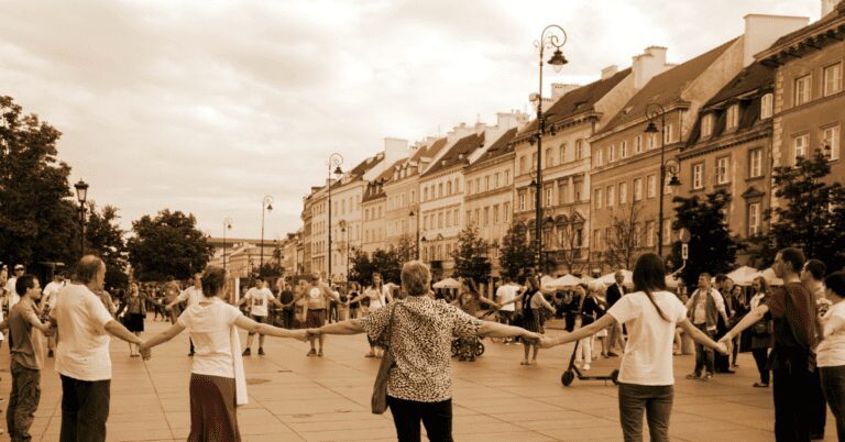 Circle of people outside holding hands on a street.