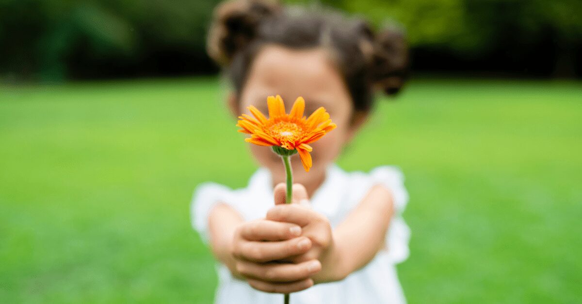 Blurred image of a little girl holding out a flower while standing on grass.