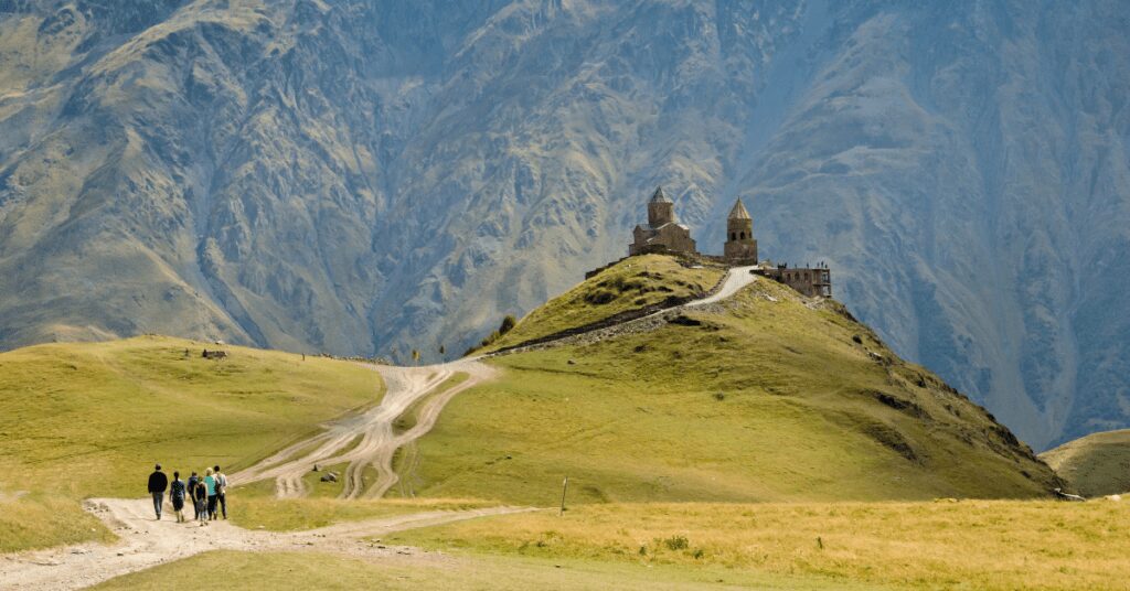 People walking on pilgrimage to a church with a mountain behind it.