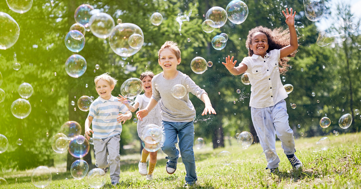 Children running outside through bubbles.