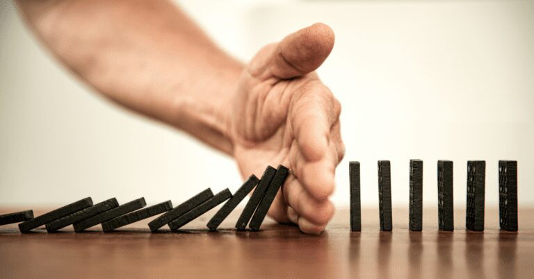 Hand stopping dominos from knocking other dominos over.