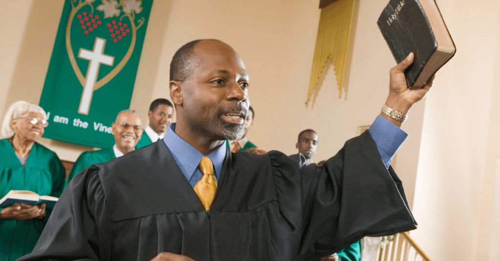 Minister in a robe holding up a Bible at the front of a church.