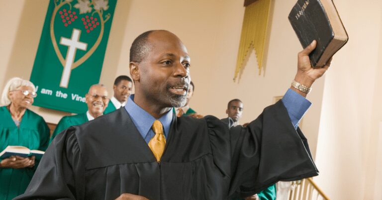 Minister in a robe holding up a Bible at the front of a church.