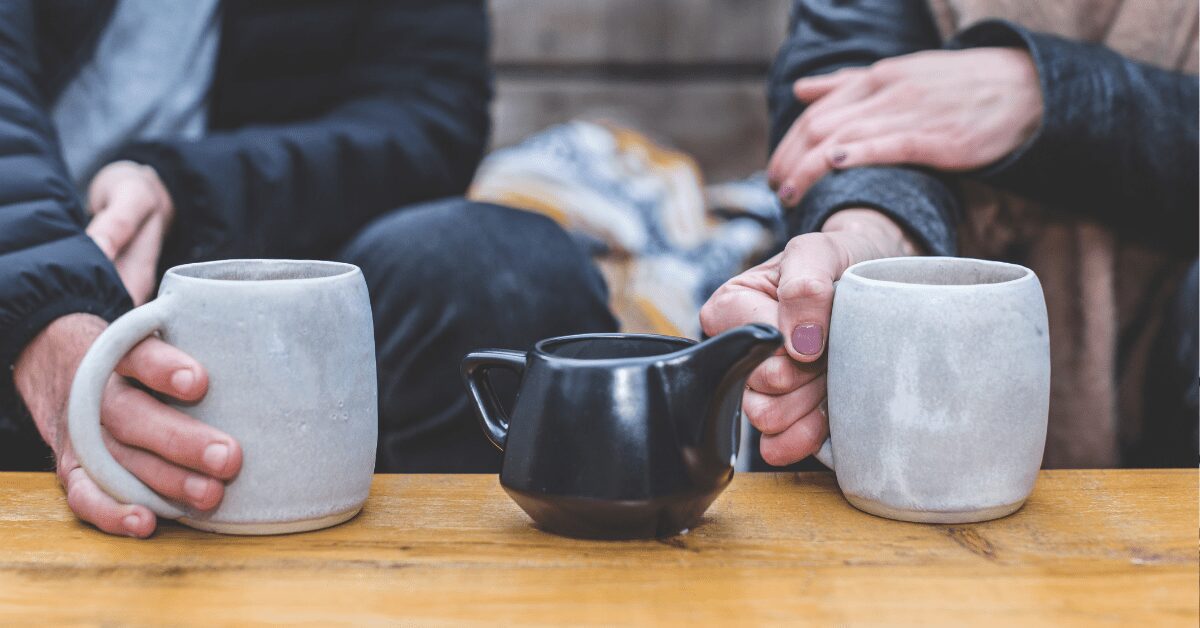 Closeup of hands holding tea cups with a small tea pot.