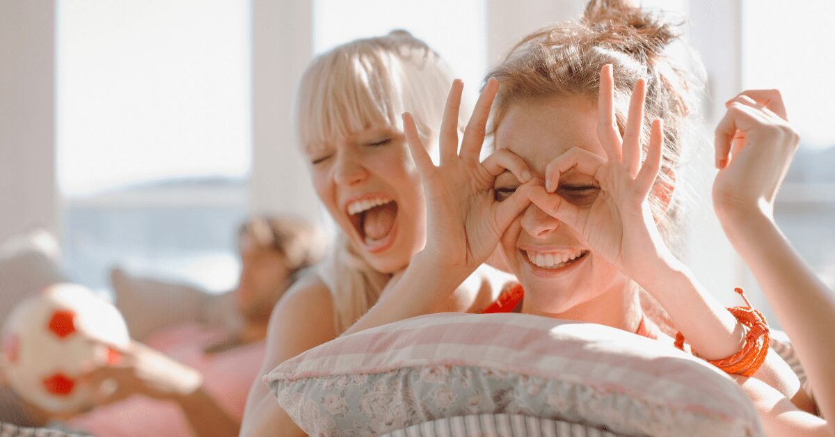 Two women laughing while one playfully covers her eyes.