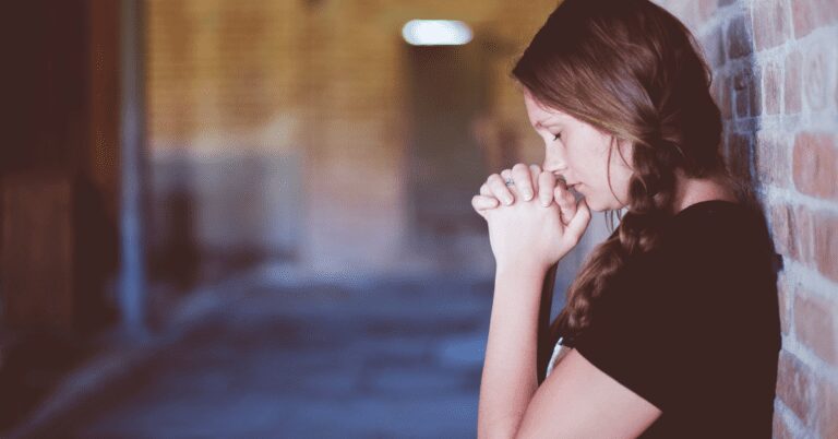 Young woman praying standing up by a wall.