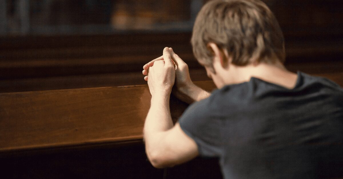 Man praying seated in a pew, seen from behind.