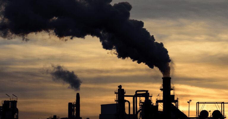 Factory smokestack at sunset producing black smoke.