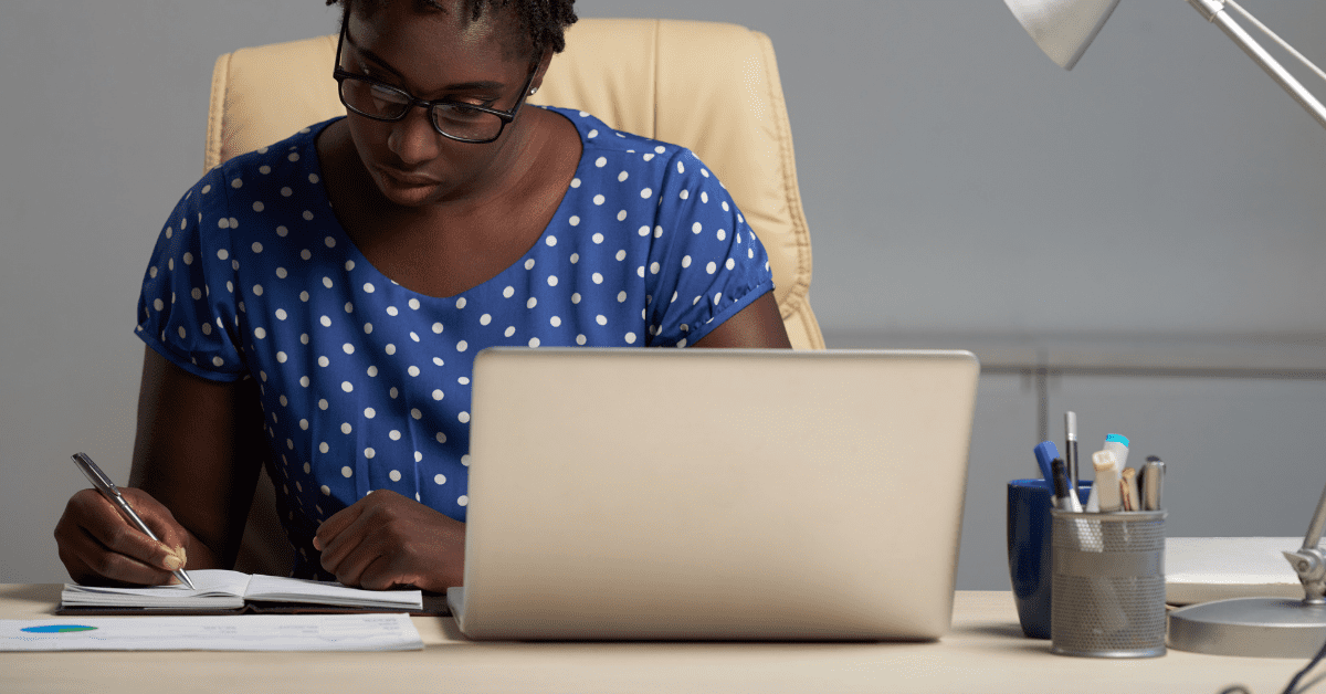Woman using a laptop and writing in a planner.