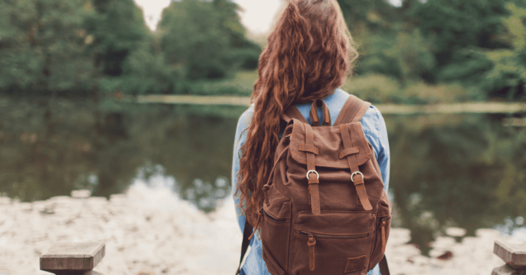 Woman sitting alone on a dock with a backpack.