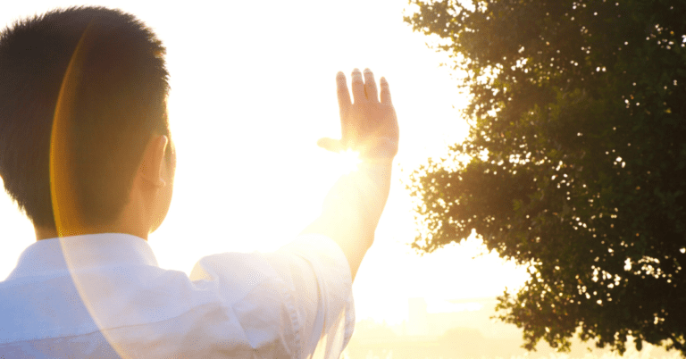 person looking up at the bright sun and shielding their eyes