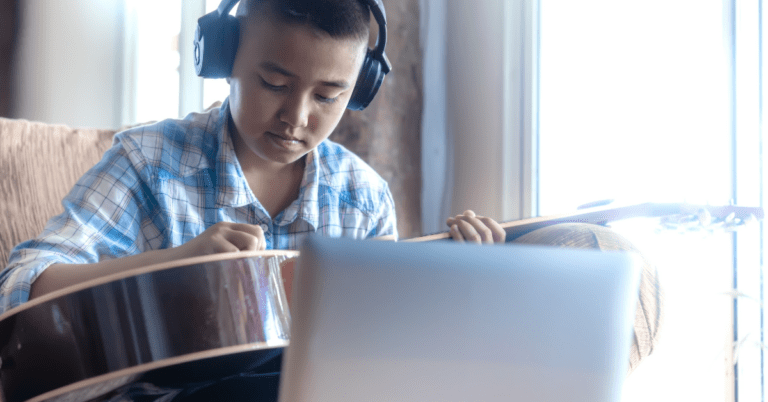 person playing guitar by their computer