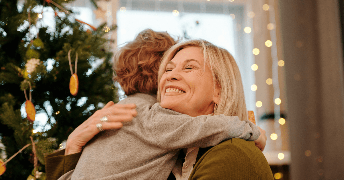 Woman hugging child in front of Christmas tree.