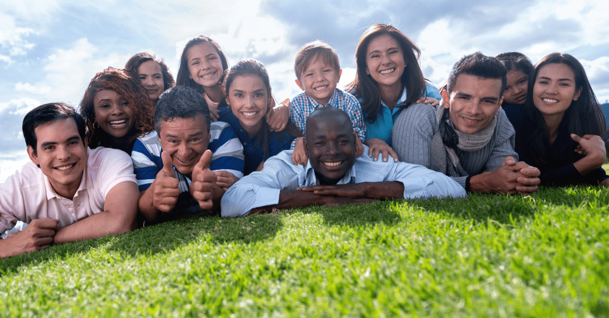 group of young people smiling while sprawled outdoors on green grass
