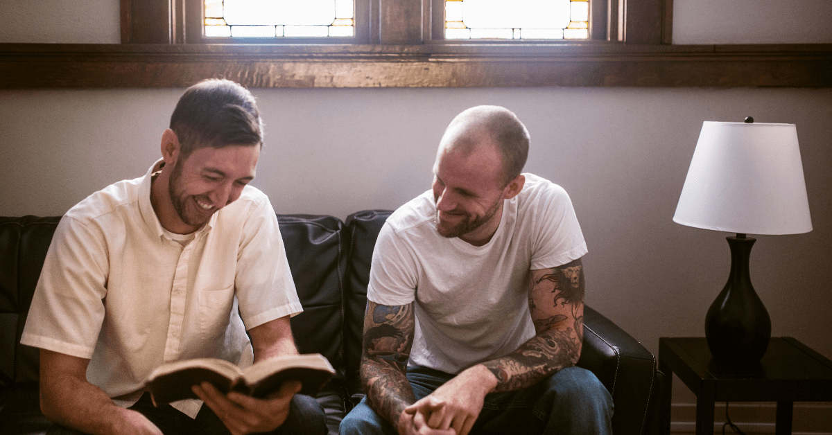 2 men smiling discussing a book being read