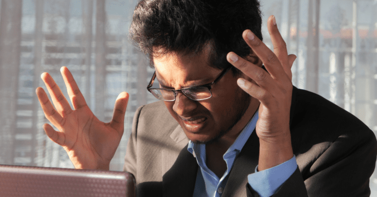 stressed man grimacing while looking at his computer