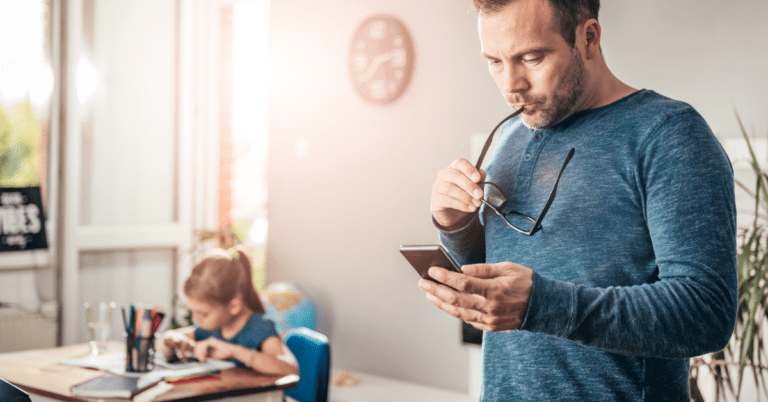 man on smart phone while daughter studies nearby