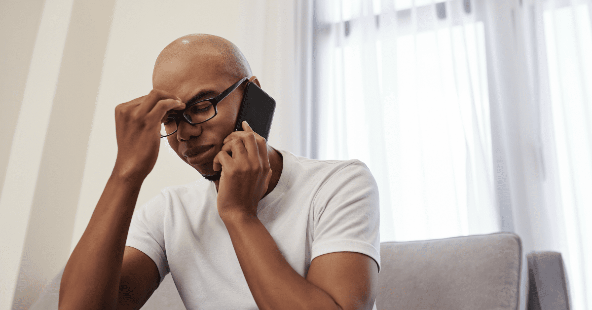 man on the phone, rubbing his forehead from stress