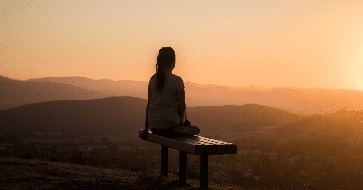 young girl sitting on a bench, watching the sunset