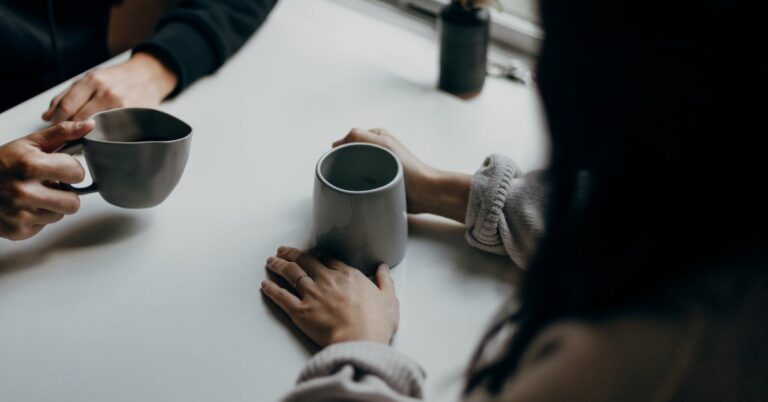 two people sitting together with coffee mugs at a table