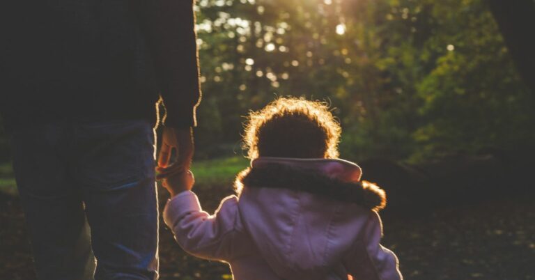 little girl in a pink coat holding her fathers hand