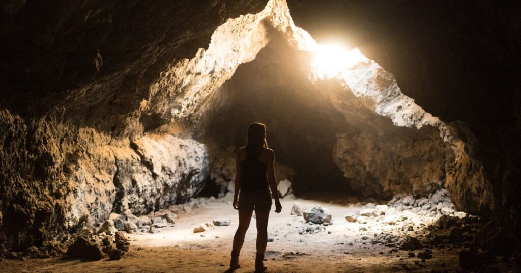 a woman exploring a cave with a crack of sunlight