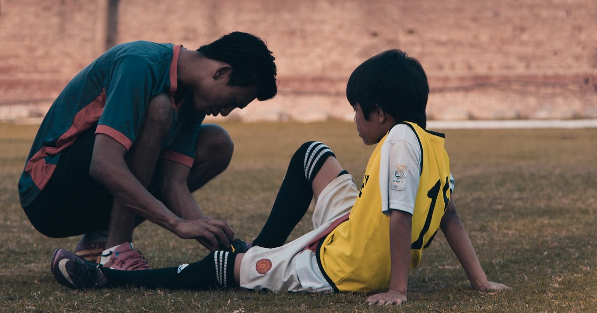 coach helping injured youth soccer player on field