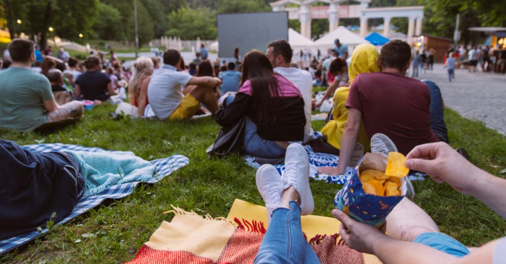 Large gathering of people sitting in a grass field in front of a movie screen.