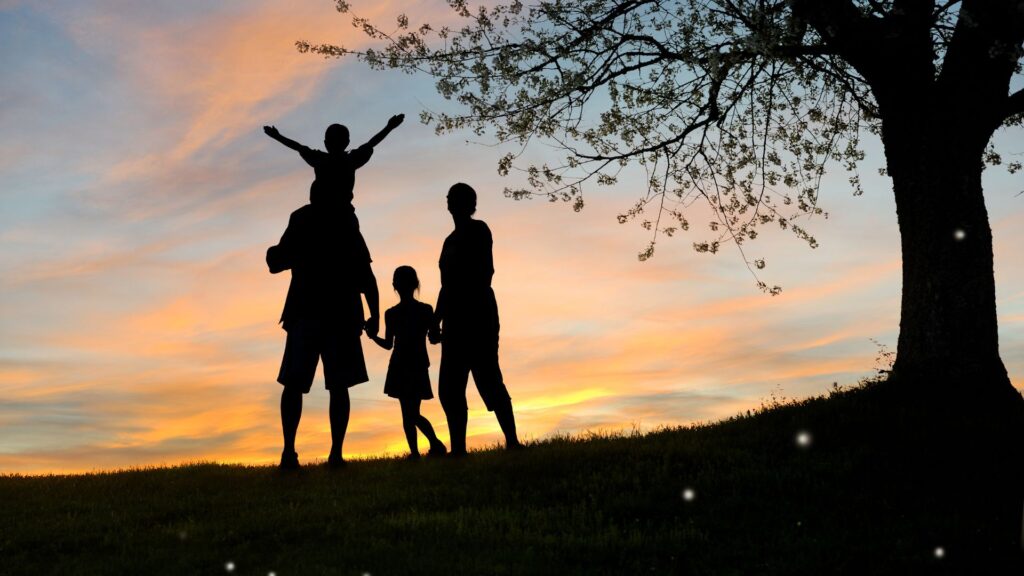 family standing next to a tree facing the sunset