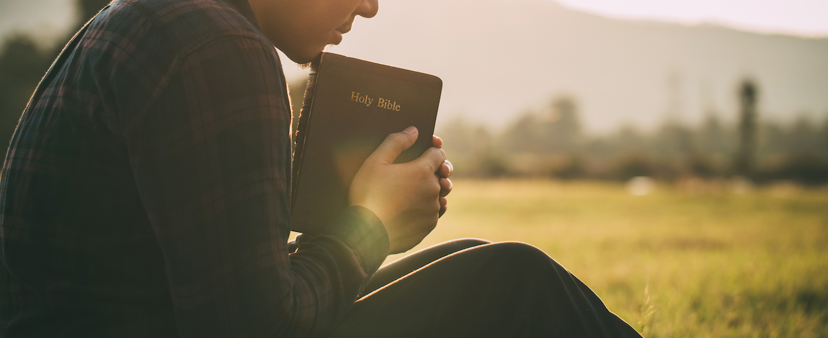 man praying holy the holy bible in a field during beautiful sunset.