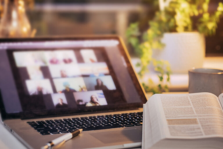 Computer, adapting technology, and the Bible on a desk at home with a videoconference on the screen in this new digital landscape shaped by a culture of social media