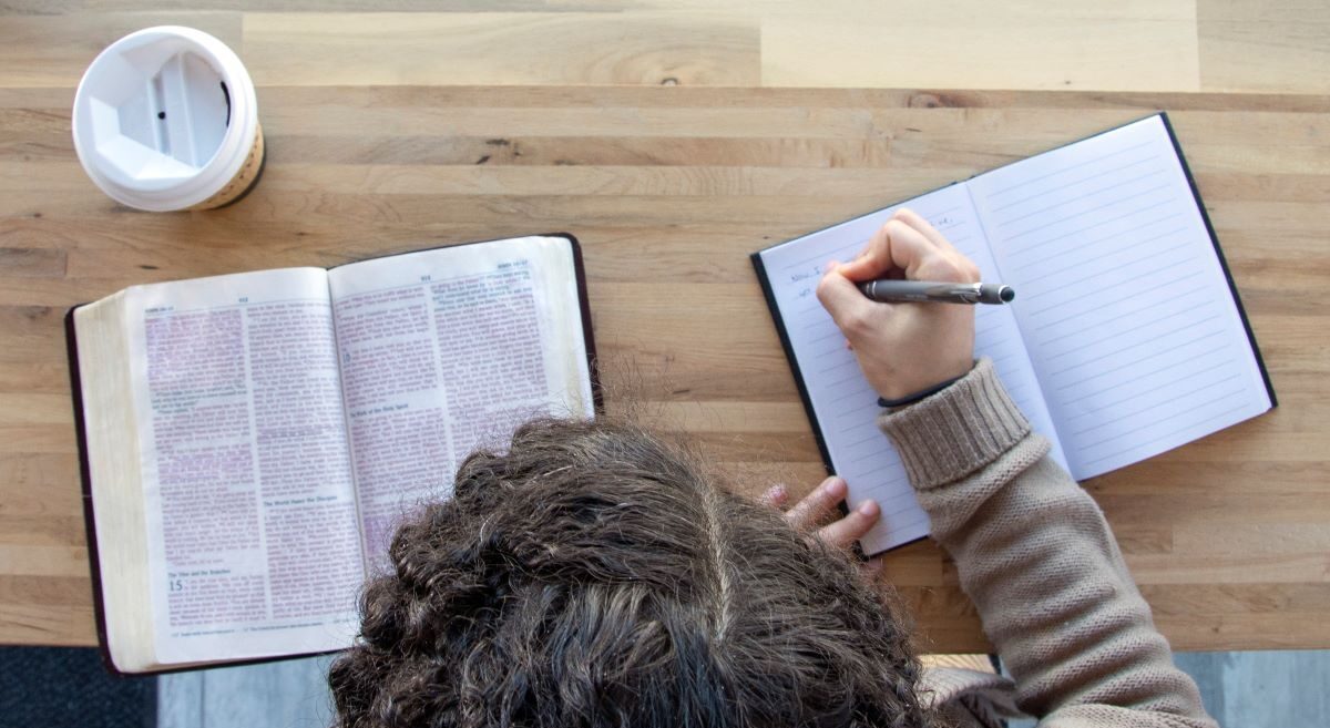 A view from above a person who is studying scripture, with a bible to their left and a notebook with notes in it to their right.