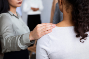 A supportive gesture in a group setting, with a woman placing her hand gently on another person's shoulder, symbolizing comfort and encouragement.