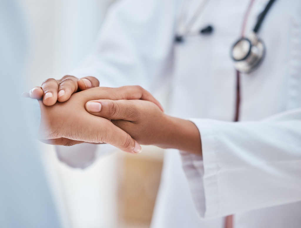 A doctor gently holds a patient’s hand, offering comfort and care during a medical consultation.