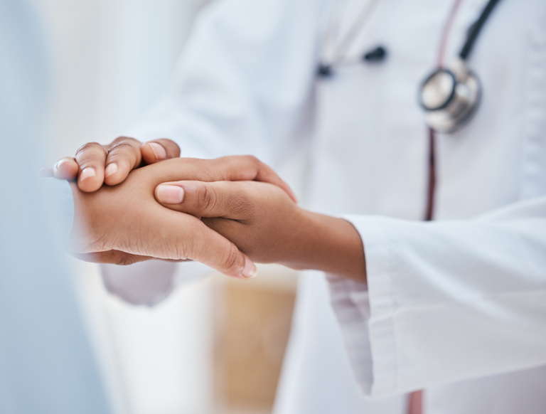 A doctor gently holds a patient’s hand, offering comfort and care during a medical consultation.