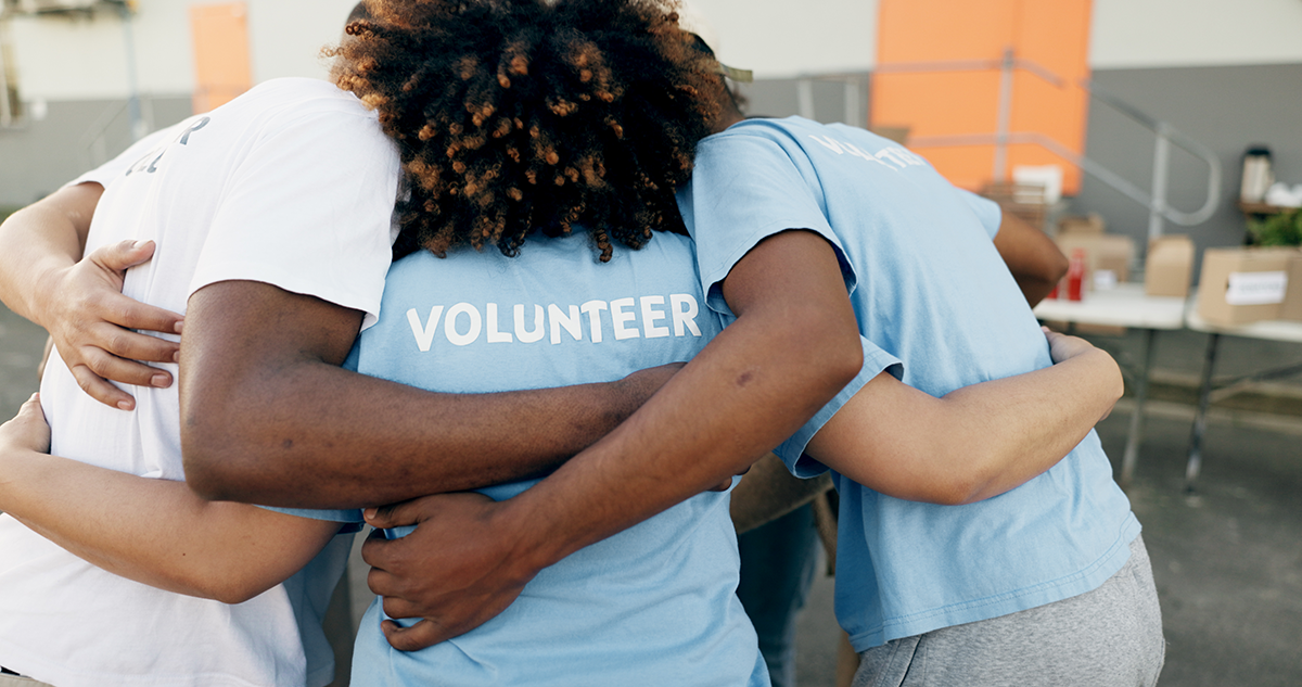 A group of volunteers in blue shirts embraces in a supportive group hug, symbolizing unity and teamwork.