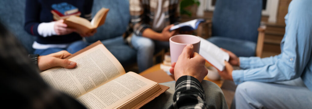 A group of people in a living room, holding books and a mug.