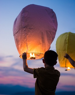Boy lofting a small hot-air balloon against evening sky