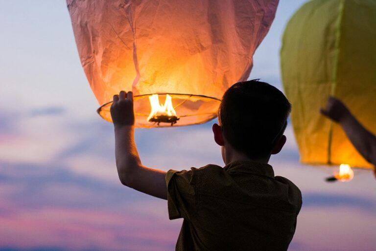 Boy releasing small hot-air balloon in front of dusky sky