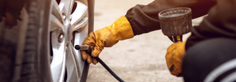 A person wearing yellow work gloves uses an air compressor hose to check or inflate the tire of a vehicle. A person wearing yellow work gloves uses an air compressor hose to check or inflate the tire of a vehicle.