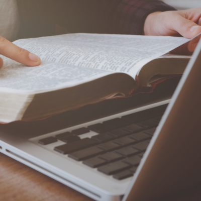 Close-up of a person holding an open book over a laptop keyboard.
