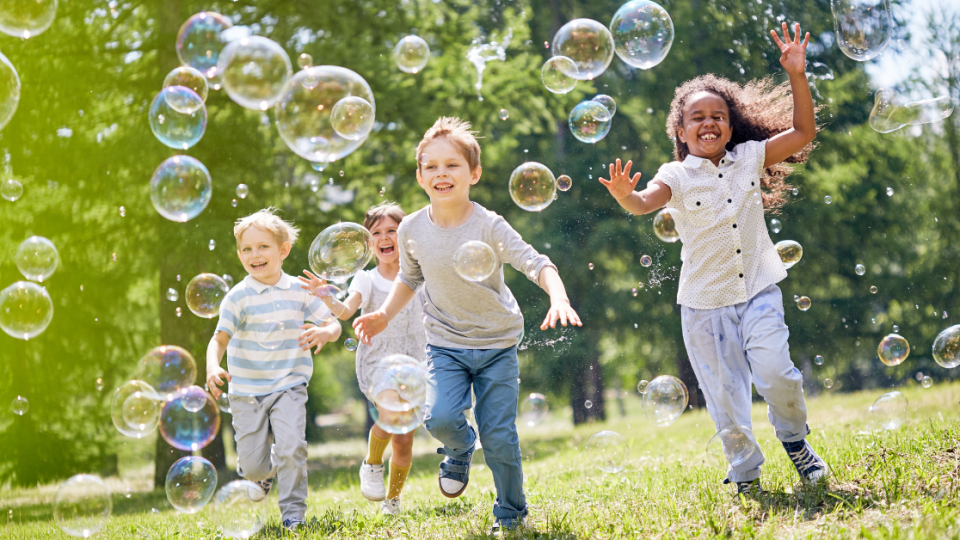 Children running outside through bubbles.