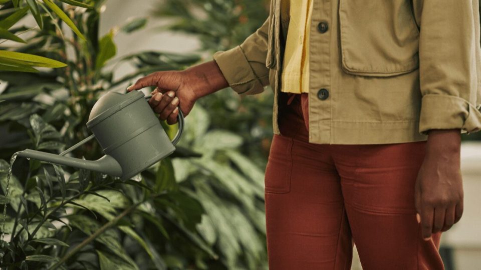 A woman watering a garden with a watering can.